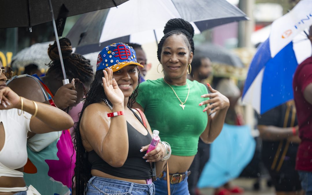 Two attendees smiling under umbrellas in the rain at an outdoor Slappers N Bangers party in Pittsburgh