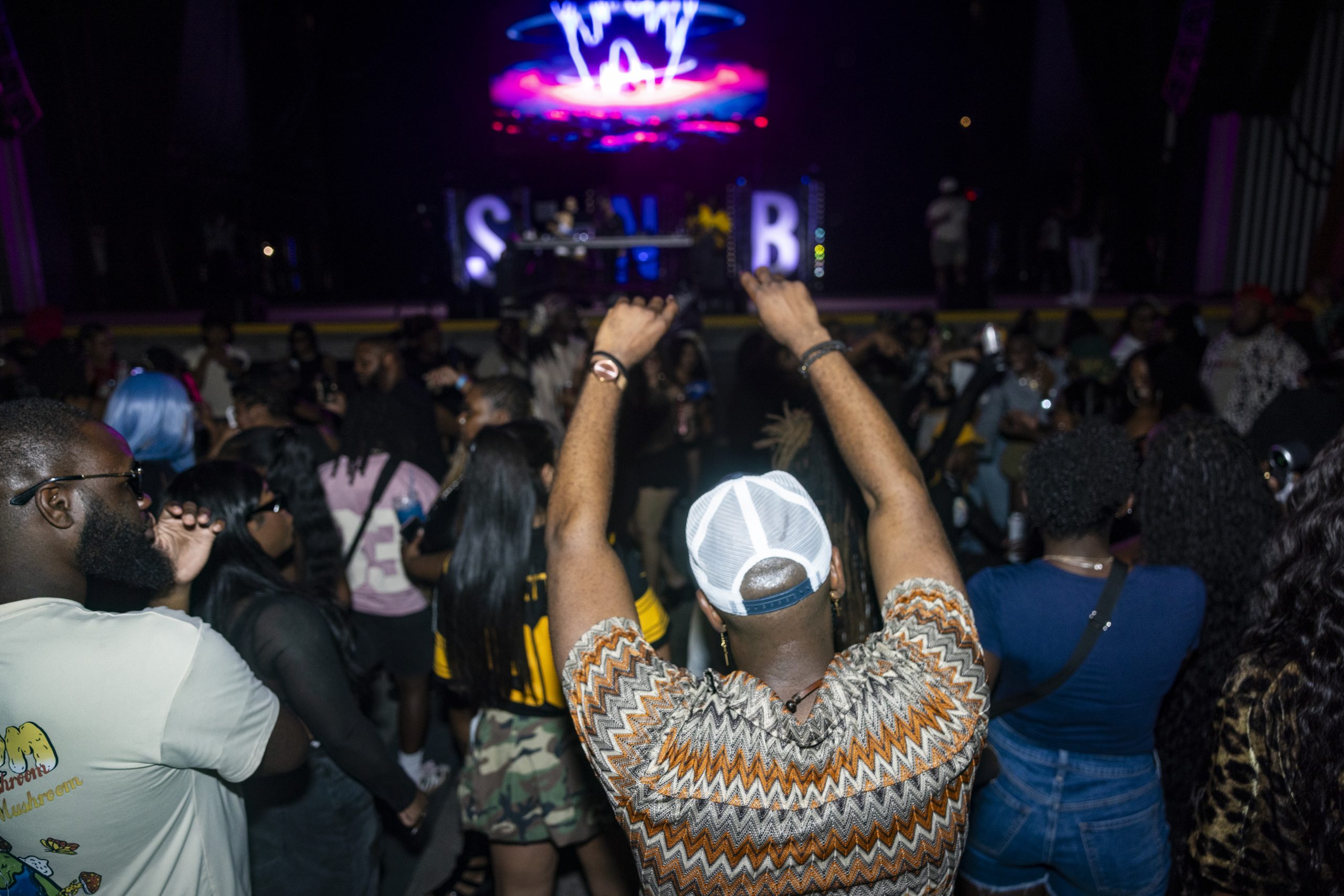 Crowd with hands in the air in front of the lit Slappers N Bangers DJ booth at a Pittsburgh hip hop party